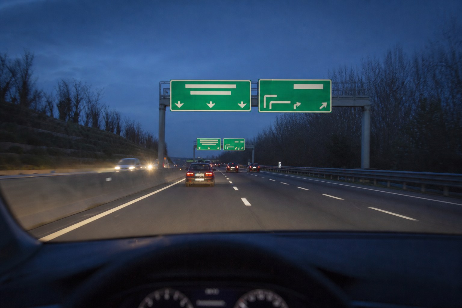 Cartelli verdi sopra un'autostrada al crepuscolo visti dal posto di guida