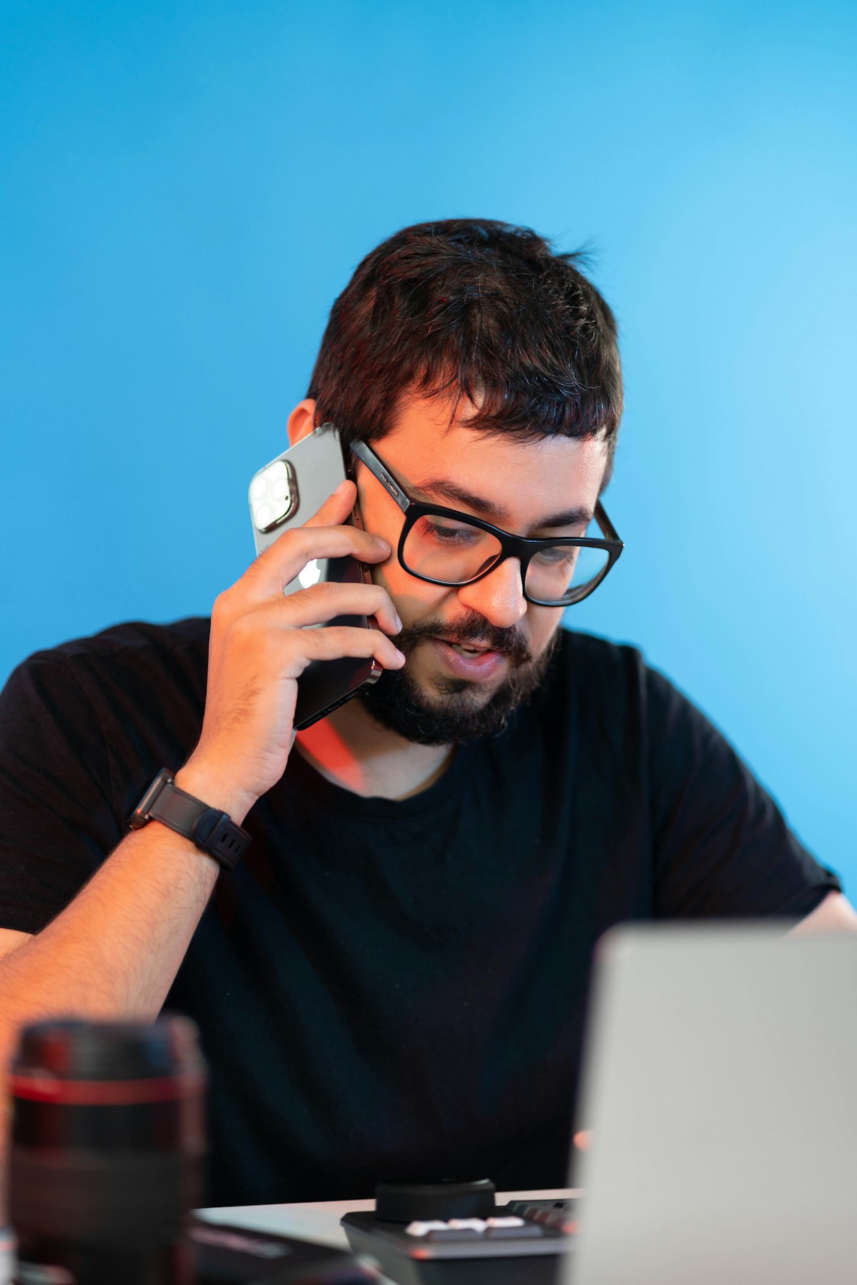 Uomo con occhiali al telefono distratto davanti al computer portatile