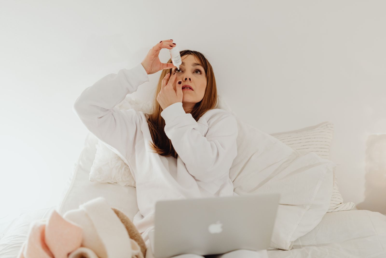 Donna che usa gocce oculari mentre lavora al computer portatile