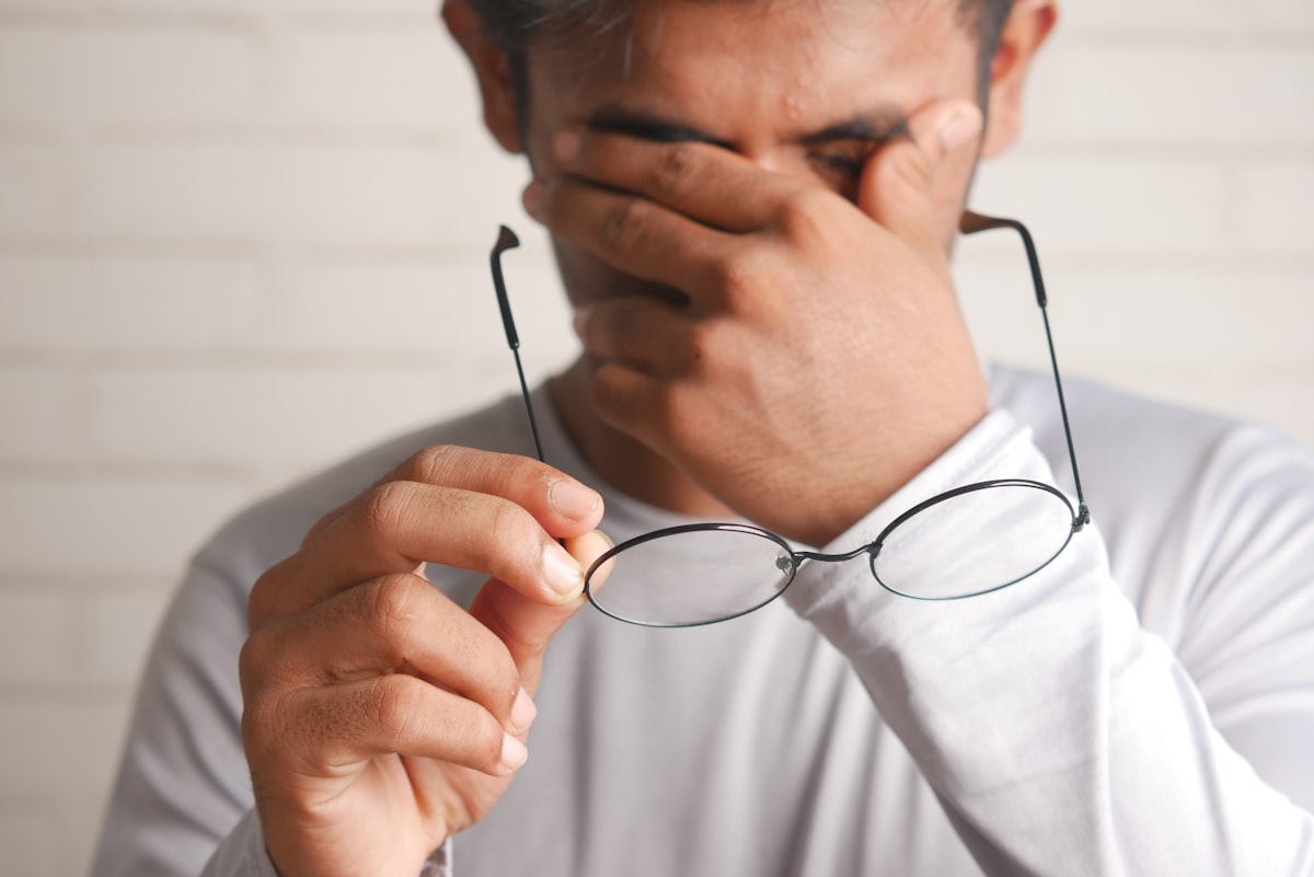 Uomo con occhiali in mano che si strofina gli occhi per il mal di testa