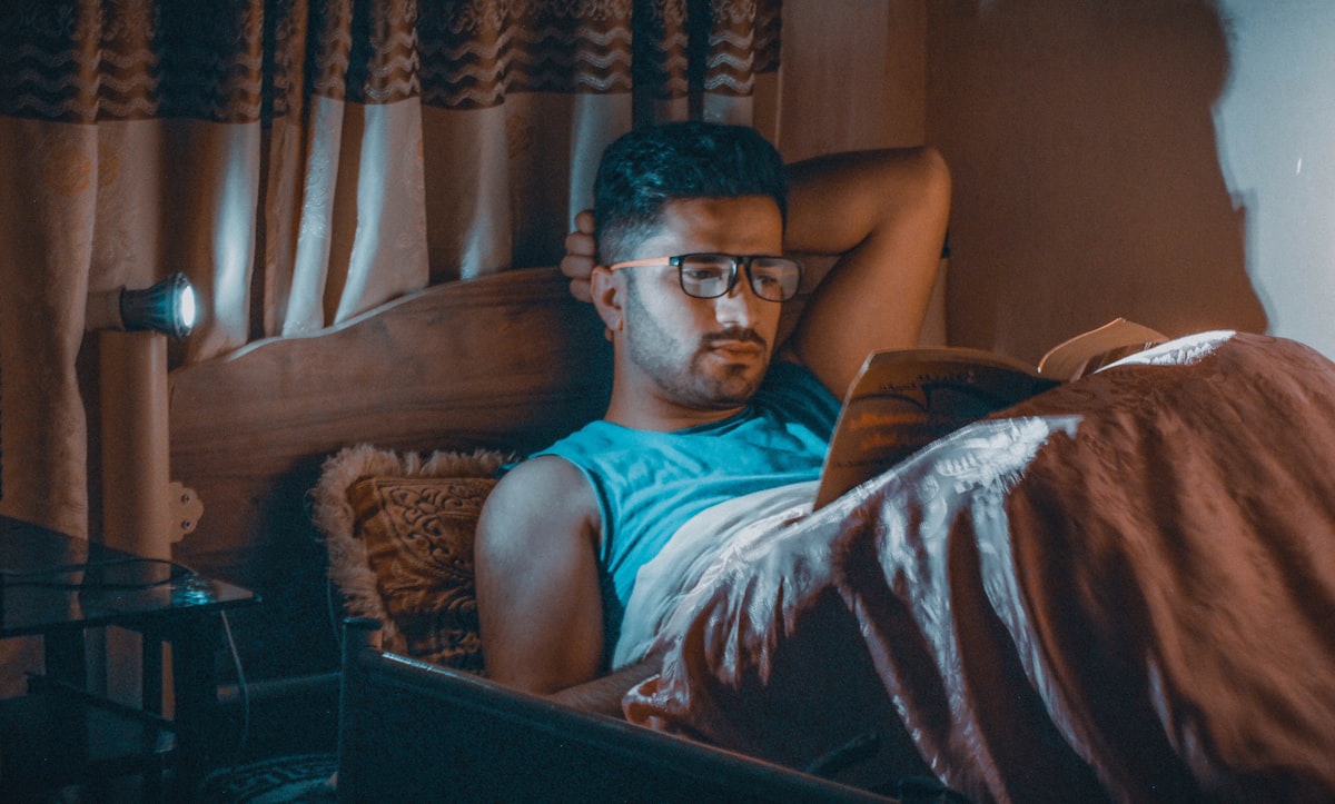 Uomo con occhiali che legge a letto di notte con luce calda