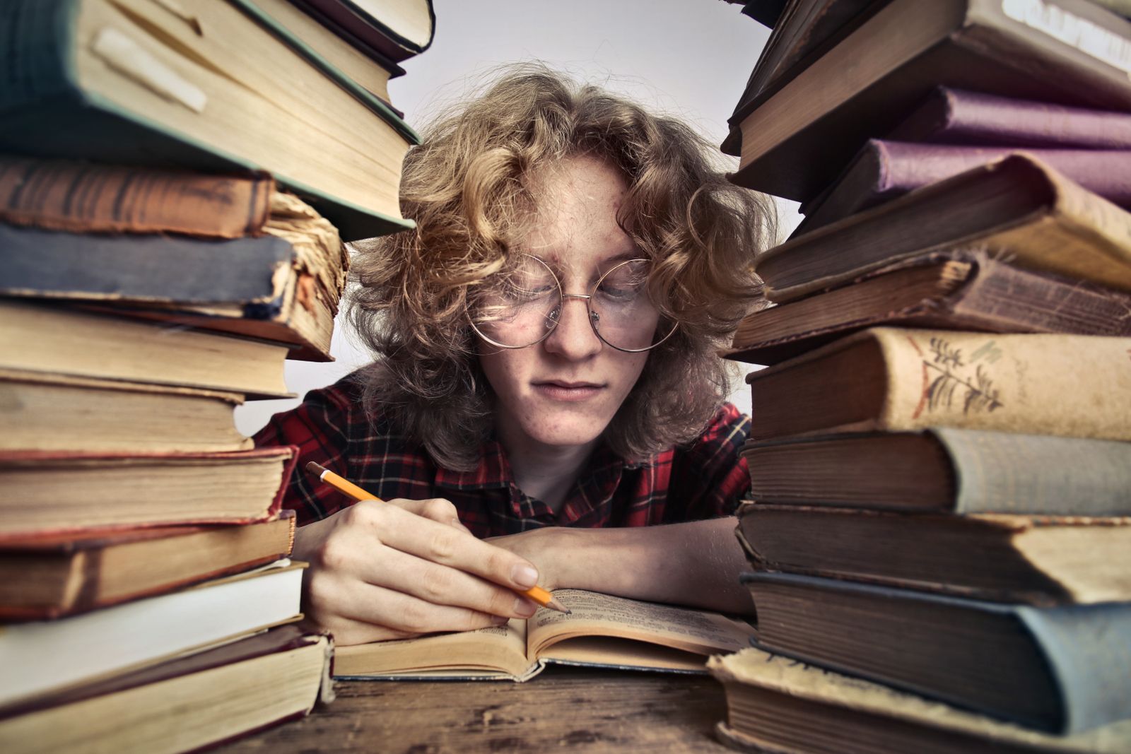 Persona con occhiali legge e prende appunti tra libri aperti