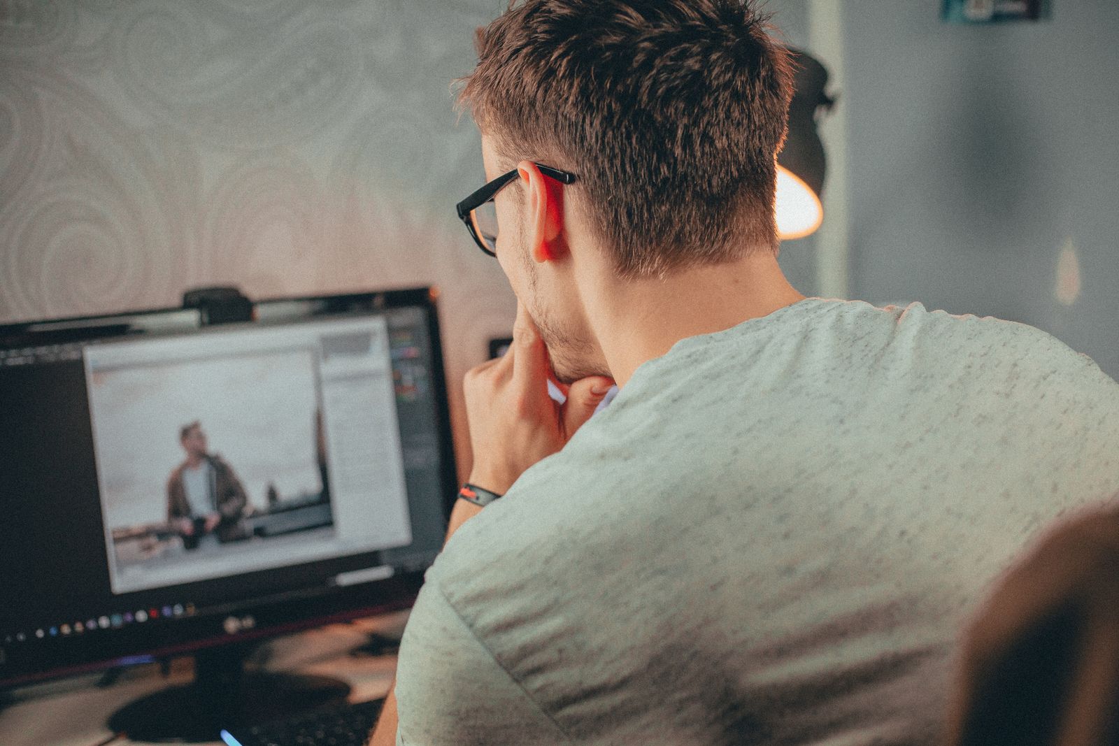 Professionista con occhiali concentrato davanti a un monitor durante un lavoro di revisione