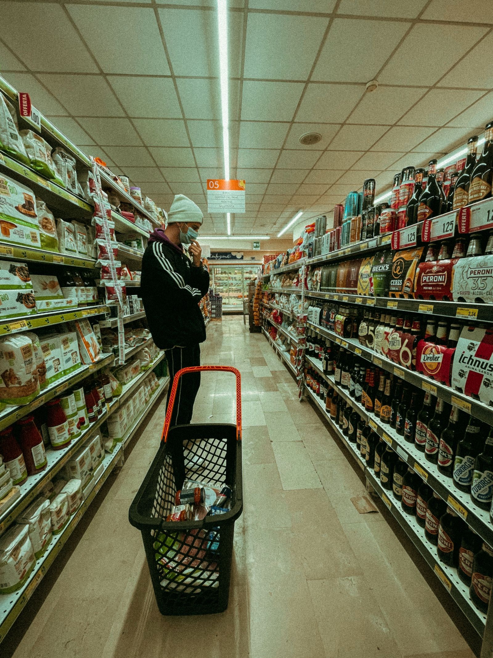 Uomo che cammina tra scaffali fitti in un corridoio di supermercato
